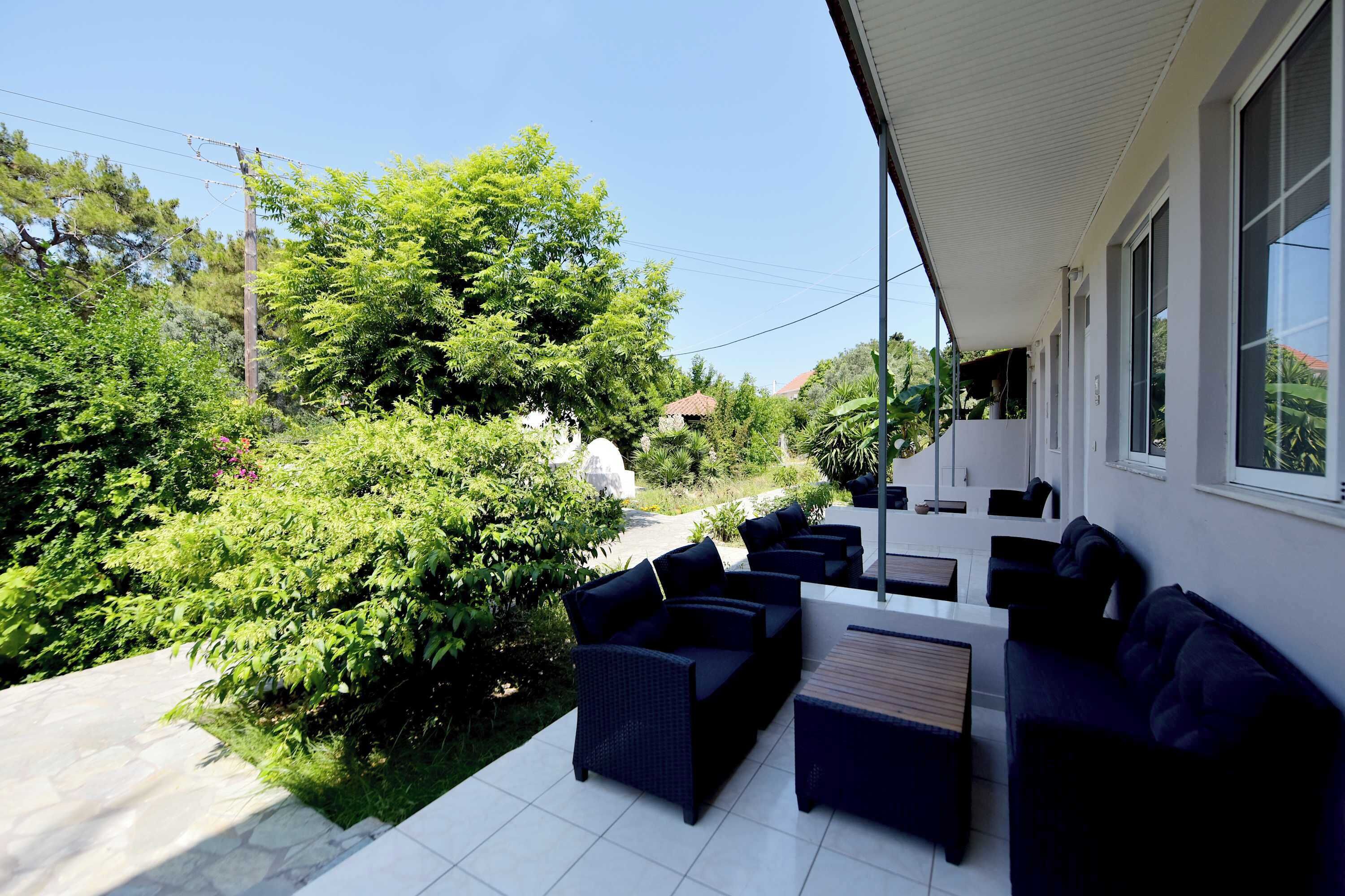 Une terrasse avec des meubles d’extérieur, un mur blanc et de la verdure.