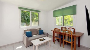 A living room with a sofa, a coffee table, and a dining table with chairs. There are windows with green blinds, and a ceiling light fixture is visible. - Dani's House (Ialysos)