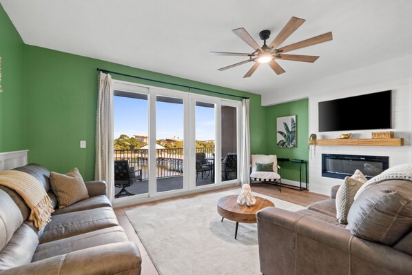 A living room with a green wall, a ceiling fan, a fireplace, and a large TV.