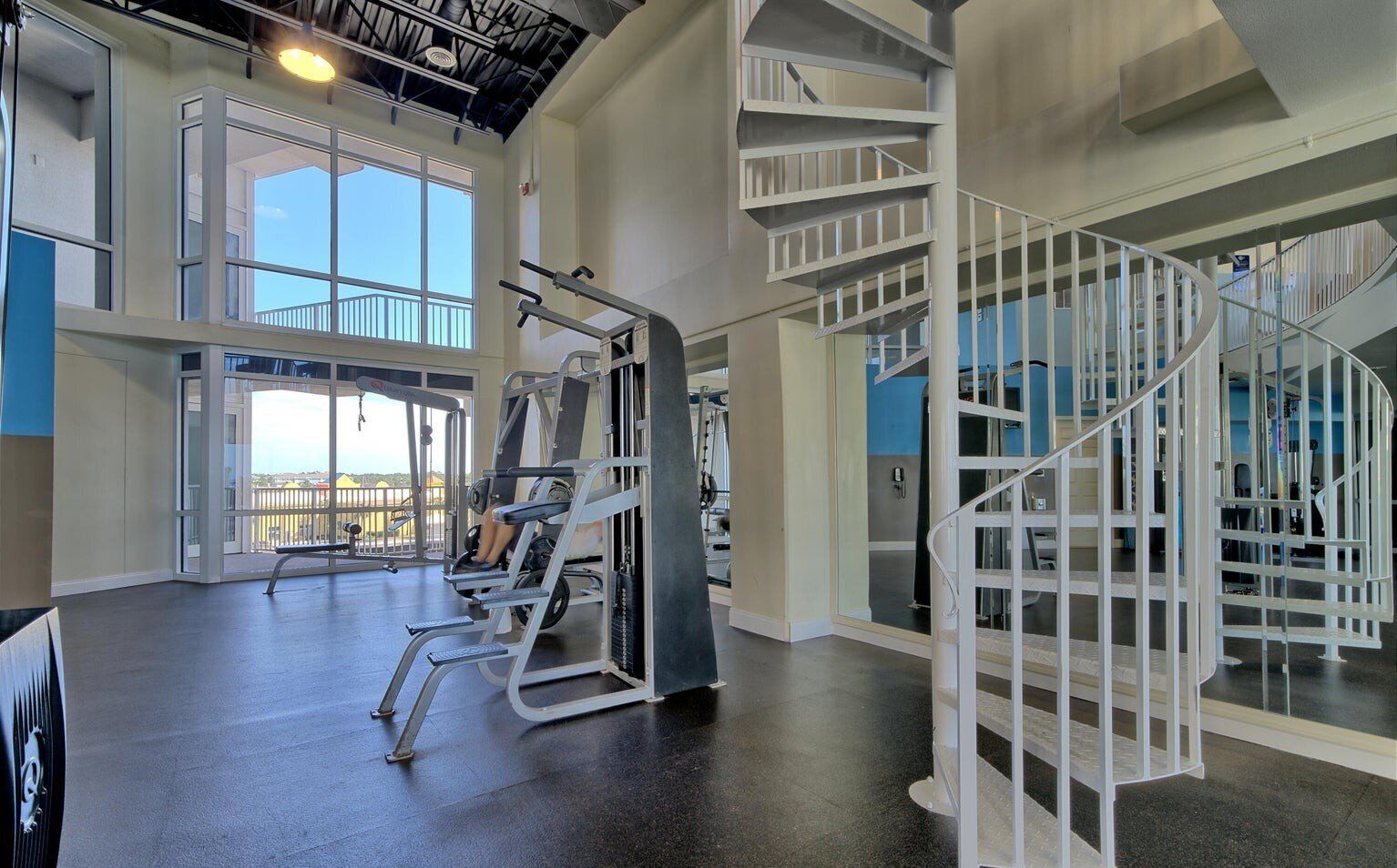 Une salle de sport équipée de matériel de musculation, dotée d’une grande fenêtre et d’un escalier en colimaçon.