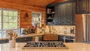A modern kitchen with dark cabinets, a gas stove, and a large window. - Slopeside Retreat, Walk to Slopes, Hot Tub, Sauna (Big Bear Lake)