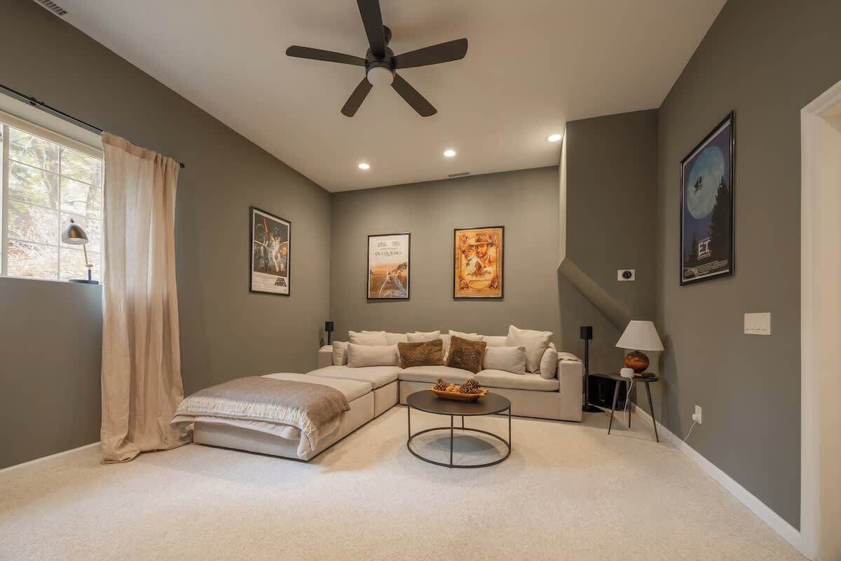 A modern living room with a sectional sofa, a round coffee table, a ceiling fan, and framed artwork on the walls.