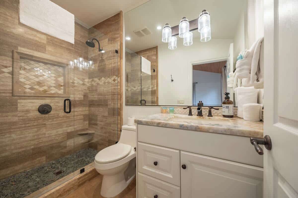 A modern bathroom with a glass-enclosed shower, a toilet, a vanity with drawers, and a mirror.