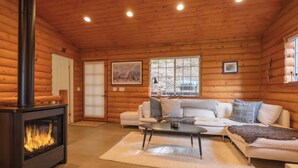 A log cabin interior with a fireplace, white sofa, and a large window. - Slopeside Retreat, Walk to Slopes, Hot Tub, Sauna (Big Bear Lake)