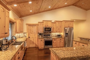 A kitchen with wooden cabinets, granite countertops, stainless steel appliances, and a wooden ceiling.