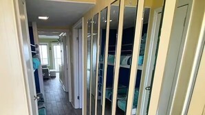 Ein schmaler Flur mit Schiebetüren zu einem Kleiderschrank, Fliesenboden und einem Bett mit blauer Bettwäsche im angrenzenden Zimmer.