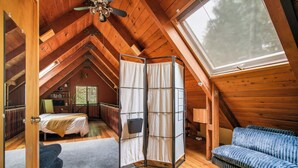A cozy attic bedroom with a sloped ceiling, a bunk bed, a sofa, and a large window providing natural light. - Storybook Mt Hood Cabin • Wood Stove + Skylights (Rhododendron)
