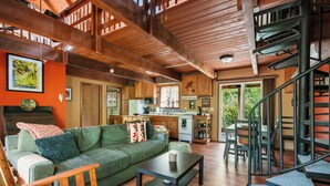 A spacious living area with a green sofa, wooden coffee table, and a spiral staircase. - Storybook Mt Hood Cabin • Wood Stove + Skylights (Rhododendron)