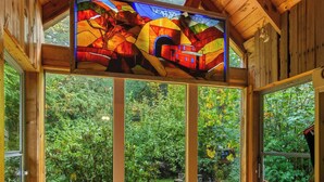A wooden interior with large windows, a stained glass window, and a wooden ceiling. - Storybook Mt Hood Cabin • Wood Stove + Skylights (Rhododendron)