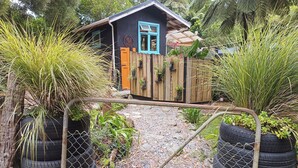 A rustic cabin with a blue door, surrounded by lush greenery and a gravel path.