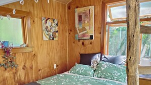 A wooden room with a bed, a window, and a painting.