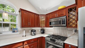 A modern kitchen with wooden cabinets, stainless steel appliances, and a large window. - 3 Bedroom Family Retreat in Ocean Pines! (Ocean Pines)