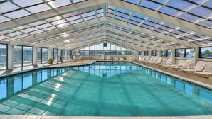 Una piscina interna con acqua cristallina, circondata da confortevoli poltrone bianche e un tetto in vetro.