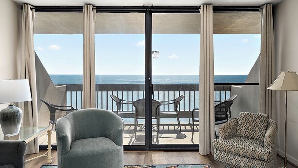 Una stanza con vista sul mare, un balcone con sedie e una poltrona a fantasia.