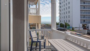 A balcony with two chairs and a table, overlooking a street and a building named "Golden Surf."