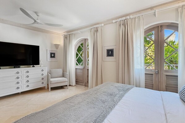 A bedroom with a bed, a TV, a dresser, a chair, and a window with curtains.