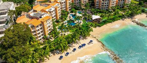 An aerial view of a resort with multiple buildings, a beach, and a swimming pool.