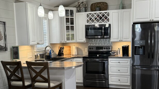 A modern kitchen with white cabinetry, stainless steel appliances, and a central island with chairs.