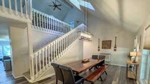 Un comedor amplio con una mesa de madera y bancos, una escalera blanca y un ventilador de techo.