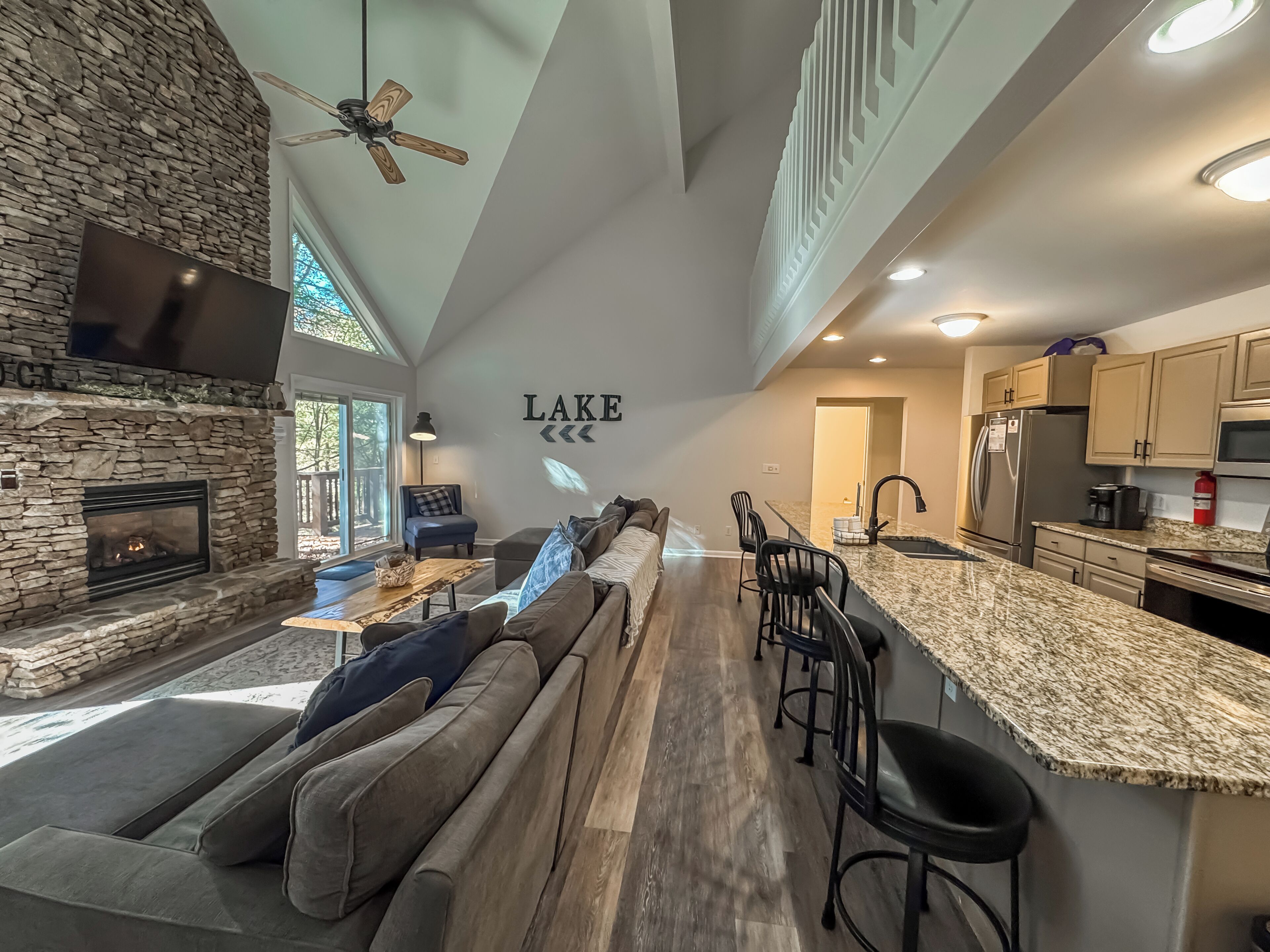 A spacious living area with a stone fireplace, a large sofa, and a kitchen with granite countertops and modern appliances.