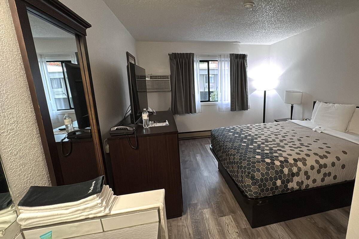 A hotel room with a bed, a desk, a mirror, a dresser, and a window with curtains.