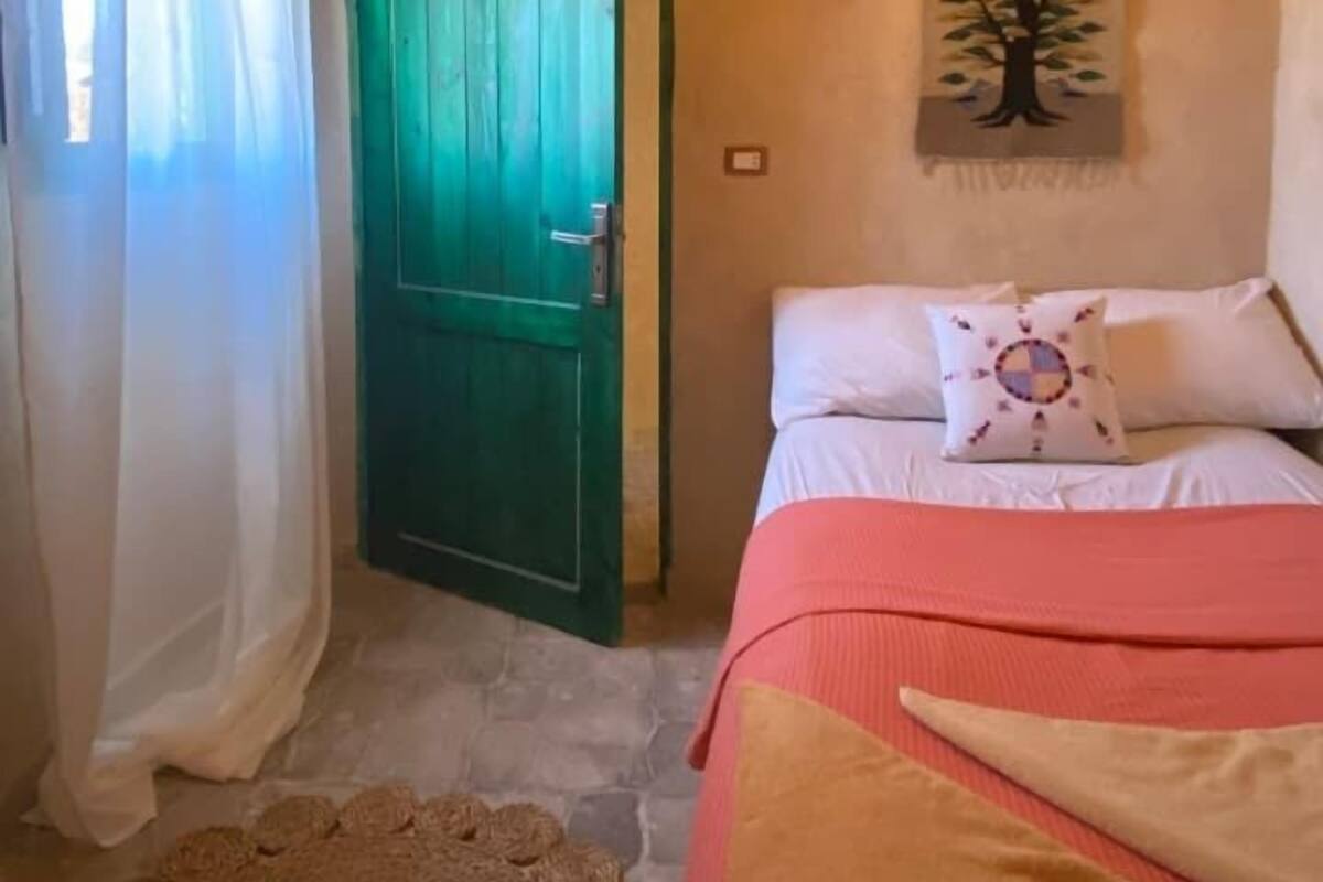 Un dormitorio con cama, una puerta verde, un cuadro colgado en la pared y techo de madera.