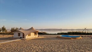 Une plage de sable avec une petite structure blanche en forme de tente et une piscine circulaire.