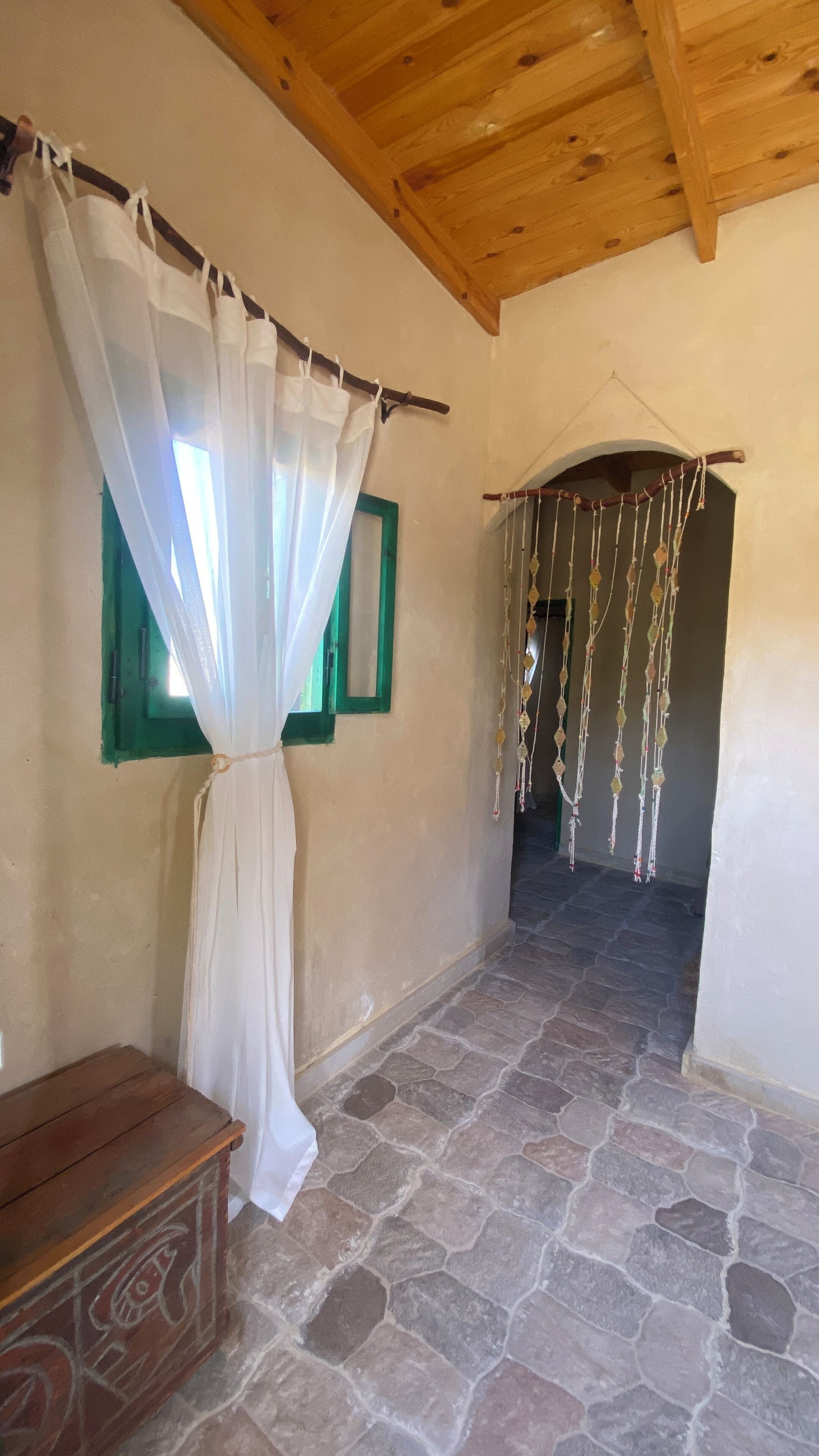Una habitación con suelo de piedra, techo de madera, cama con dosel blanco y un adorno colgante.