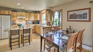 A modern kitchen with wooden cabinets, a dining area with a wooden table and chairs, and a large window with curtains. - Paradise Found Condo with Stunning Mountain Views located in Paradise Valley, MT (Emigrant)