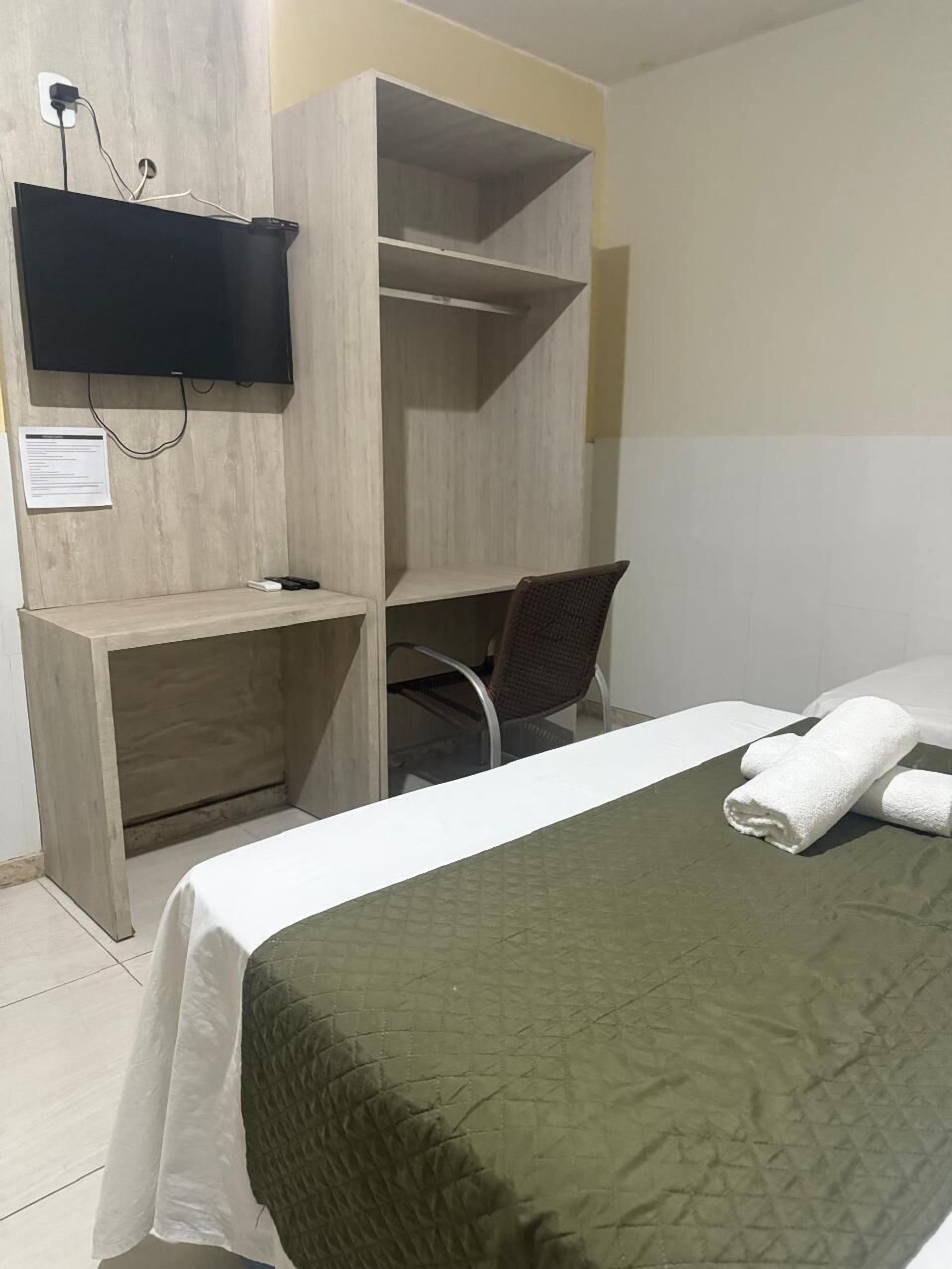 Una habitación de hotel con una cama, un escritorio, una silla y un televisor montado en la pared.