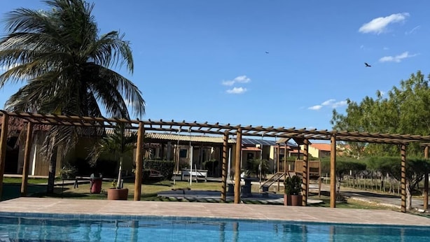 A swimming pool with a wooden pergola and palm trees in the background. - HOTEL XIQUE XIQUE POUSADA (Piranhas)