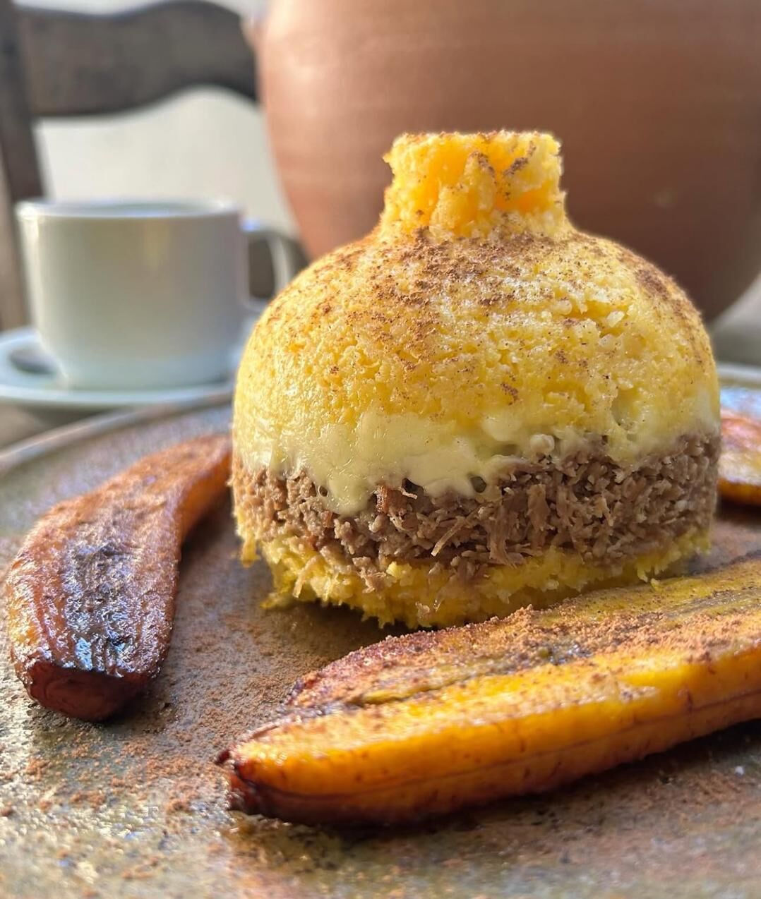 Un alimento con corteza dorada, relleno blanco y centro oscuro, acompañado de una banana y una taza.