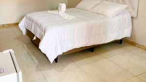 A neatly made bed with a tufted headboard, a folded towel on the bed, and a small round decorative item on the wall. - HOTEL XIQUE XIQUE POUSADA (Piranhas)