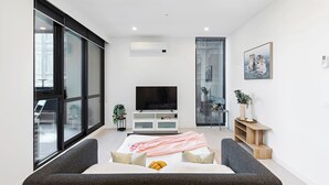Ein modernes Wohnzimmer mit großem Flachbildfernseher, einer Couch, einem Couchtisch und einer Glastrennwand.