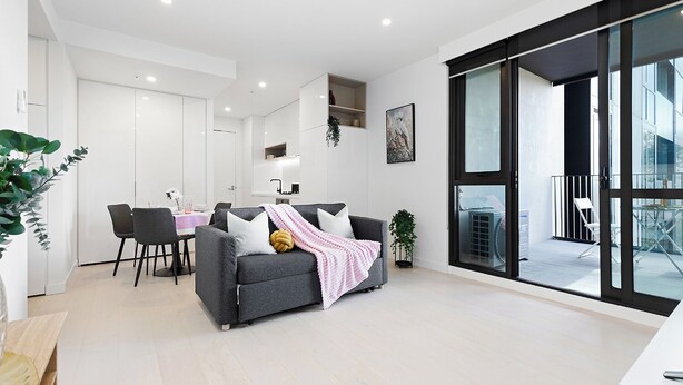 Ein modernes Wohnzimmer mit grauem Sofa, einem Esstisch mit Stühlen und einer großen Glastür, die zu einem Außenbereich führt.