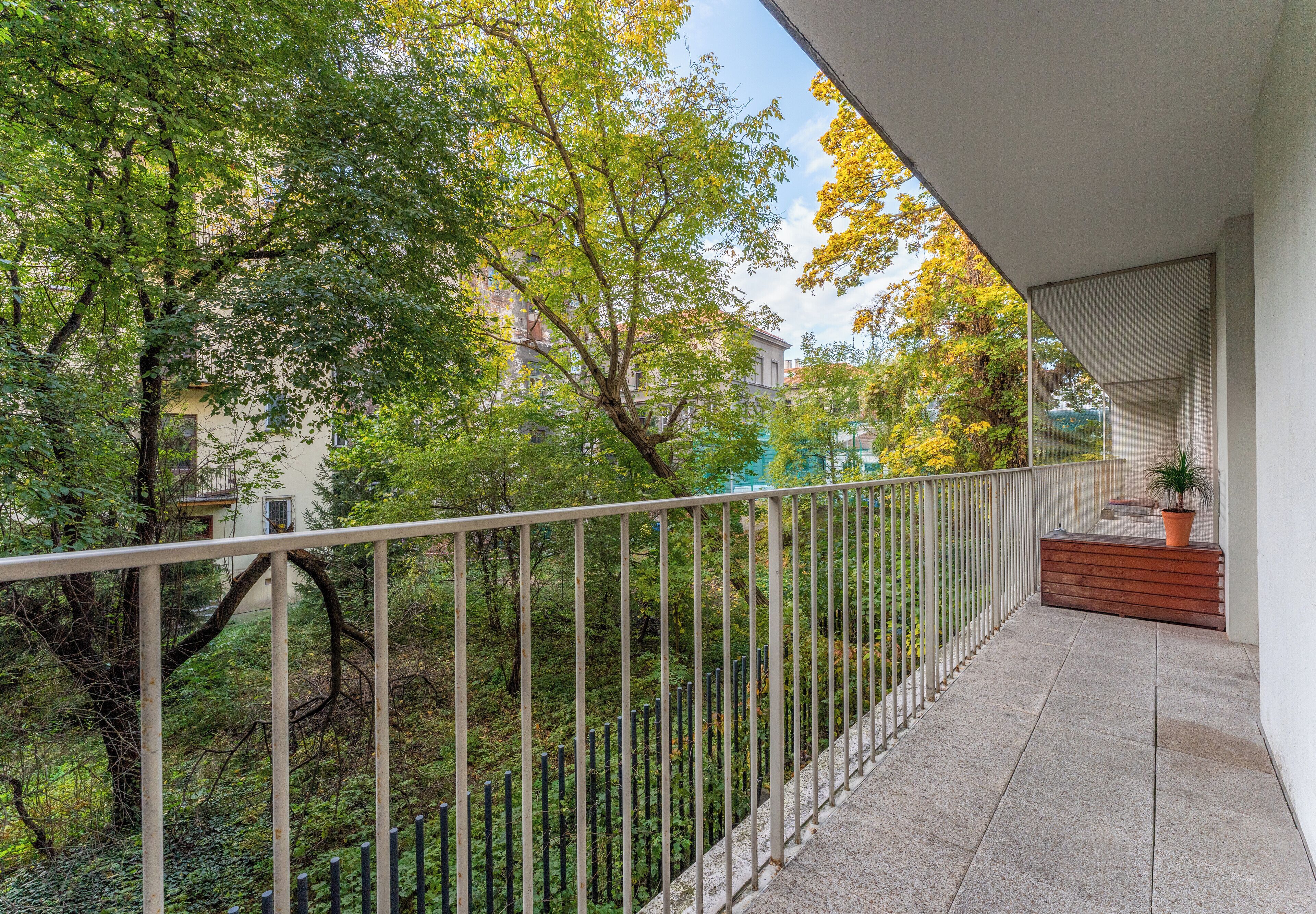 A balcony with a metal railing, a potted plant, and a wooden bench.