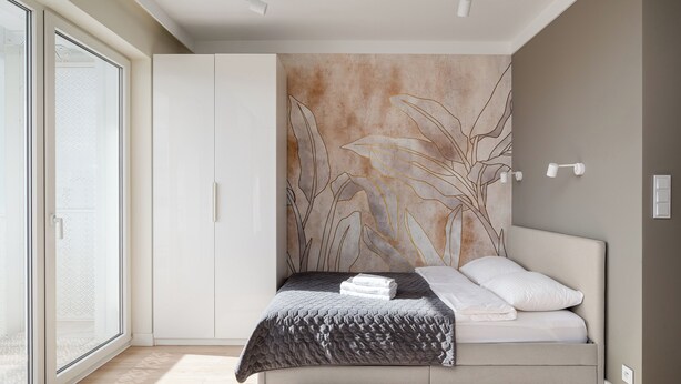 Une chambre moderne avec un lit, une grande fenêtre et un mur orné d’un motif de feuilles.