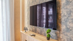 Un saló modern amb una taula consola de fusta, un televisor de pantalla plana muntat a una paret amb textura, una petita planta en test i una escultura d'arbre decorativa.