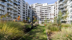 Un edifici modern d'apartaments amb nombroses balcons, un pati central amb gespa i plantes, i un cel serè.