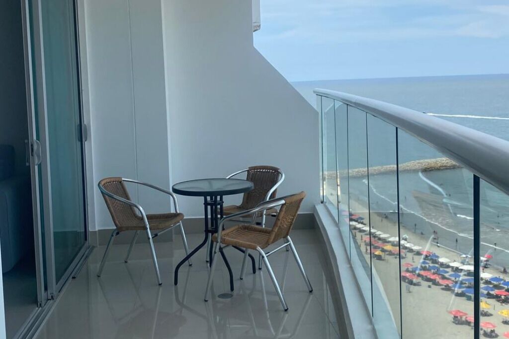 A balcony with a glass railing, a round table, and four wicker chairs.
