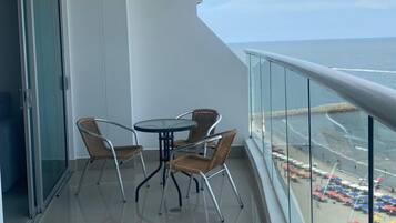 A balcony with a glass railing, a round table, and four wicker chairs.