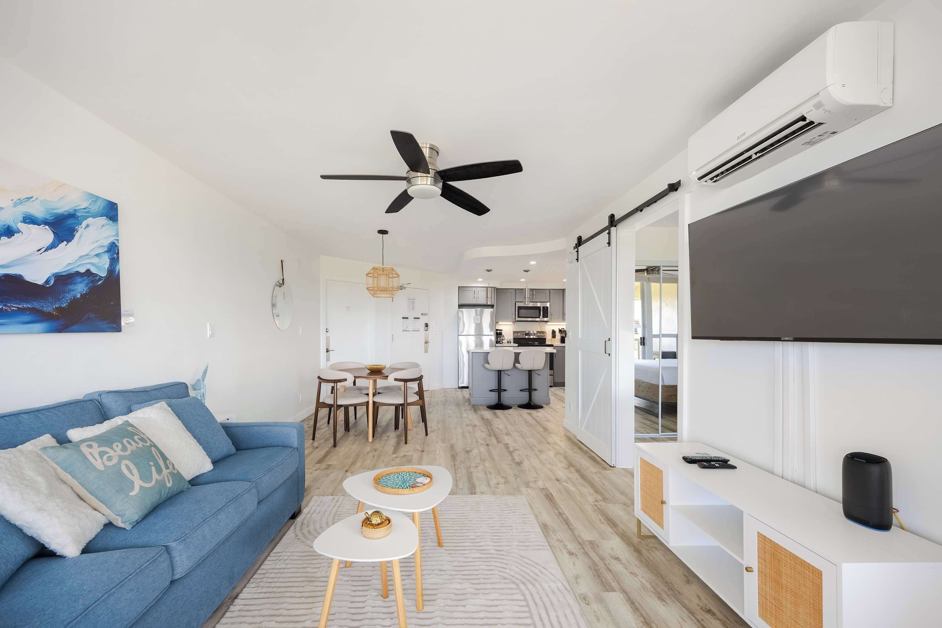 A modern living room with a blue sofa, a dining area, a kitchen, and a mounted TV.
