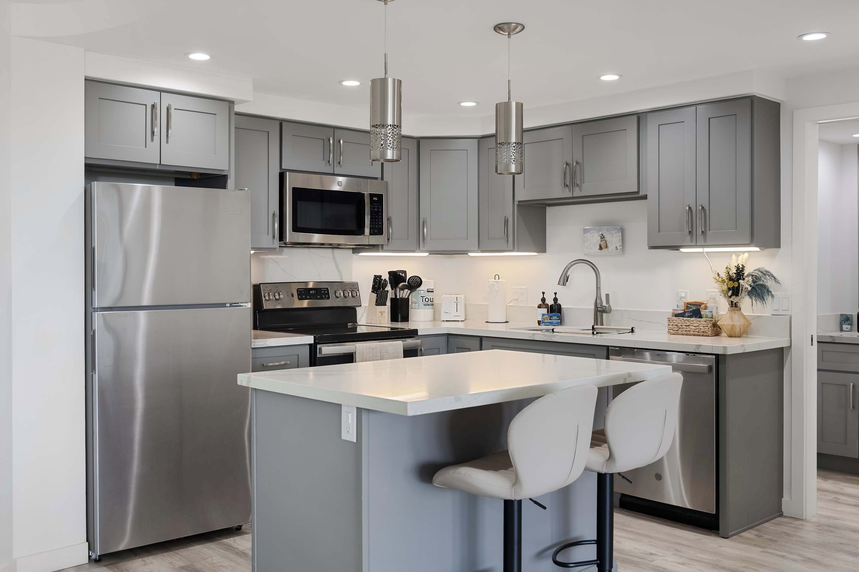 A modern kitchen with grey cabinets, stainless steel appliances, a central island with bar stools, and pendant lighting.