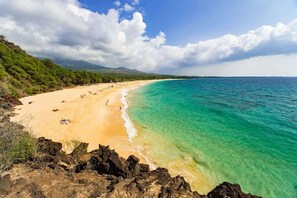 Een strand met helder turquoise water, een zandstrand en rotsachtige uitstekenissen.