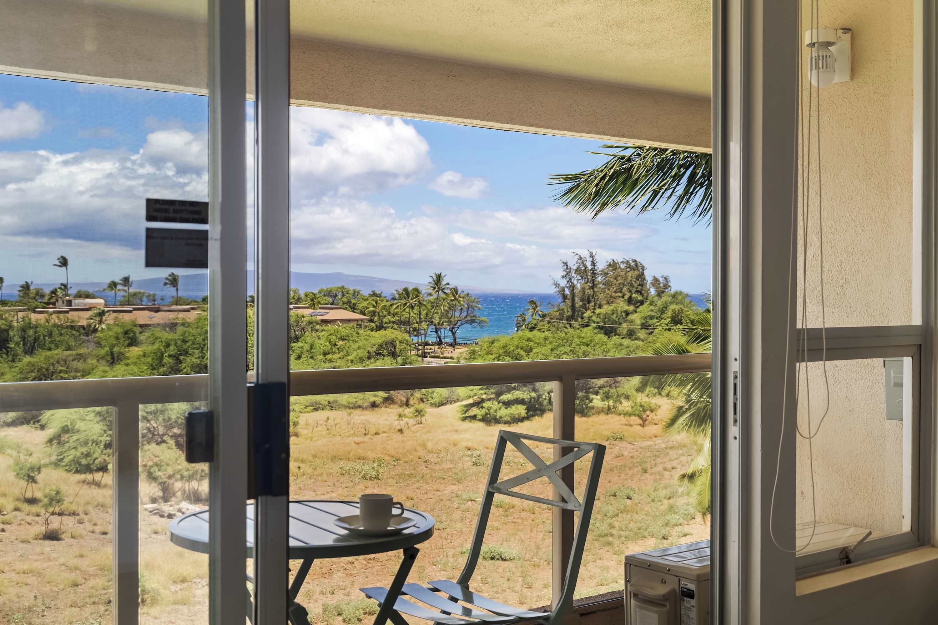Ein Balkon mit Tisch und Stuhl, der einen Blick auf eine Landschaft mit Bäumen und den Ozean bietet.