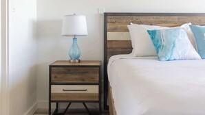 Cama bem arrumada com cabeceira de madeira, mesa de cabeceira com abajur e um conjunto de gavetas.