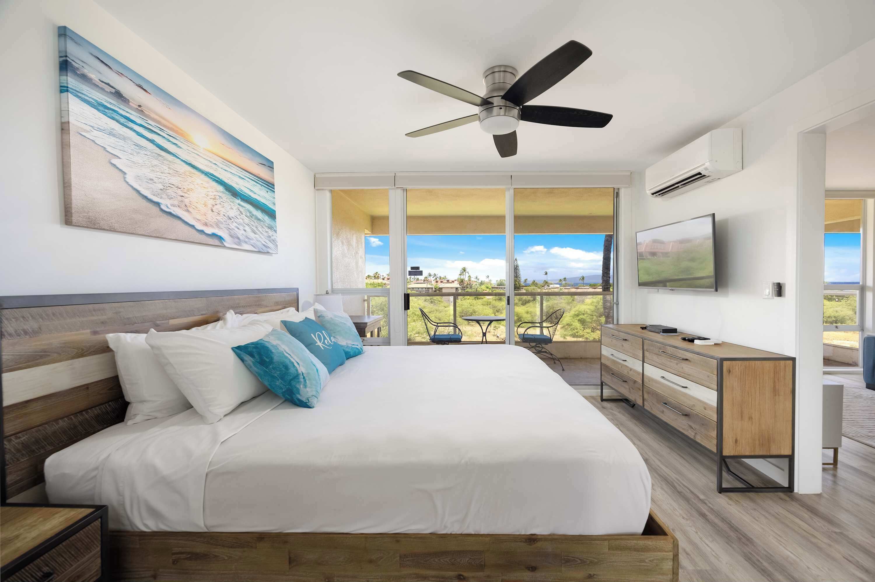 Ein Schlafzimmer mit Bett, Deckenventilator, Fernseher und Balkon mit Blick.