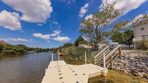 A wooden dock extending into a calm body of water, with a stone wall and stairs leading up to a building.