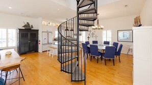 A spacious living area with a spiral staircase, a dining table with blue chairs, and a kitchen area with white cabinets.