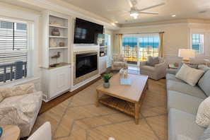 A living room with a fireplace, television, and a view of the ocean. - Bellissimo - Oceanfront with Pool, Hot Tub, Theater Room, Elevator, Game Tables (Virginia Beach)